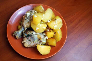 stewed potatoes with chicken and garlic in a ceramic plate on a wooden background
