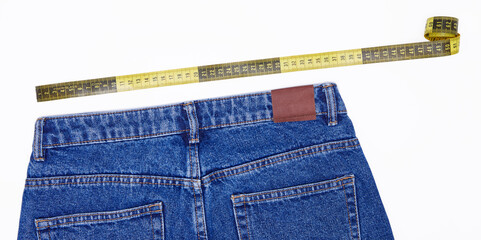 Blue jeans being measure by a yellow and black measuring tape, against white background