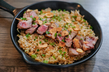 Beef with garlic fried rice, a Japanese dish consisting of a bowl of rice topped with rare beef served on a black pan