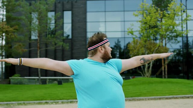 Handsome obese guy doing yoga outside at fresh air beside of a modern building he are very excited he start to loose the weight