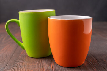 Big green and orange mugs on wooden background, front view.
