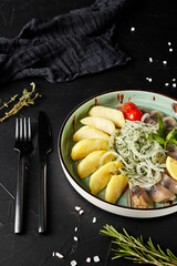 herring, potatoes and onions in a plate on a black textured background with a fork and spoon