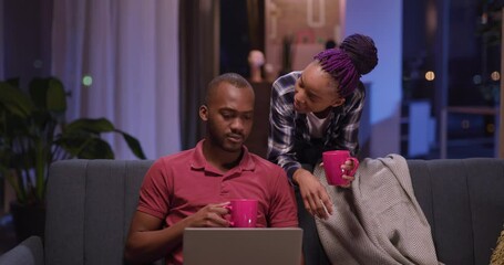 African american dating lo0ve couple of woman and man staying home using laptop working in evening communicating together. - Powered by Adobe