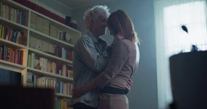 Cinematic shot of young carefree happy smiling homosexual female gay and transgender man couple in love is enjoying time together and having fun to dance together while listening to the music at home