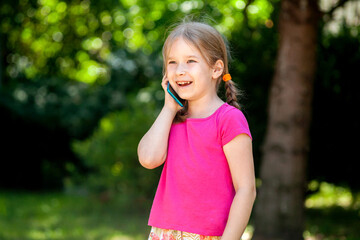 Happy cheerful little girl, child talking on phone laughing, young kid with a smartphone, phone call outdoors, portrait, copy space Telecommunication, mobile phone communication concept lifestyle shot