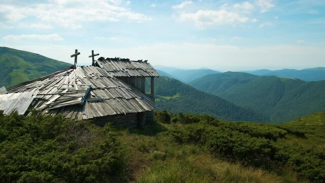 Summer mountain landscape with old forsaken tourist shelter on grassy hills and distant peaks at colorful day.