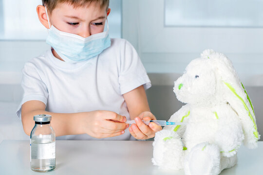 Vaccination and immunization of population concept. Kid boy in medical protective mask plays,  inoculate  stuffed animal. Little doctor, new Normal.