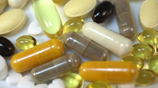 White, yellow, brown, transparent, black, oval and oblong tablets, pills, capsules smoothly rotate in the frame. Close-up, real time, on a white background