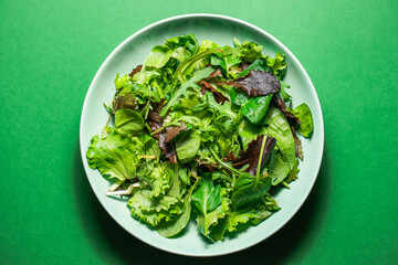 Healthy fresh salad of spinach, arugula, mini romaine lettuce, batavia salad in a green plate on a green background. Food background for menu, recipe. Top view. salat with green leafs