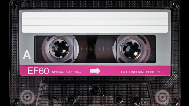 Audio cassette tape in use for sound recording in the tape recorder. A vintage pink and white, brand new blank labelled music cassette playing back in a deck player. Static video camera shot. Close up