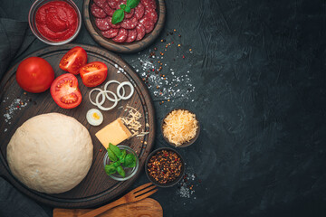 Dough, salami, tomatoes, cheese, basil and spices on a black background. Ingredients for pizza.