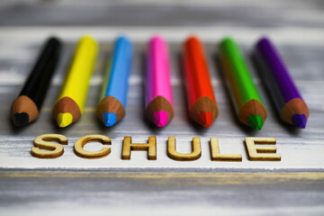 Closeup of row multi colored crayons on wood table with german word schule (english meaning: school)