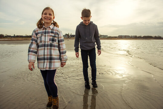Two happy teenager children siblings walking on Baltic sea beach in spring