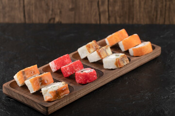 Wooden plate of traditional sushi rolls on black table