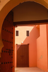 View beyond wood door and arabian style arch into bright sunny empty yard of riad in red orange...