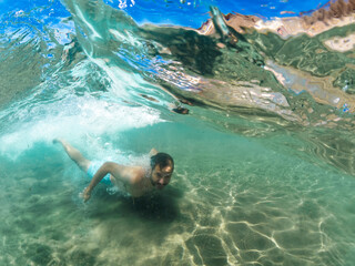 Young man swimming in crystal clear waters of the Mediterranean Sea with underwater camera