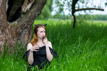 Young beautiful witch in black dress conducts a ceremony in a green forest on a summer day. Modern witchcraft.