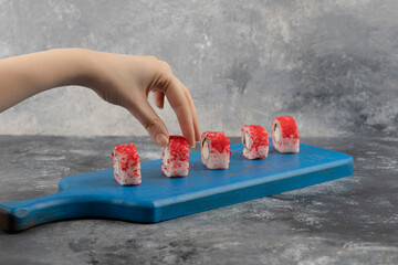 Female hand picking red sushi roll from blue cutting board © rastockinc