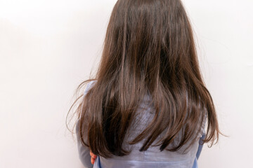 Obraz premium A small child with long brown hair turned away from the camera. Girl looking face to wall