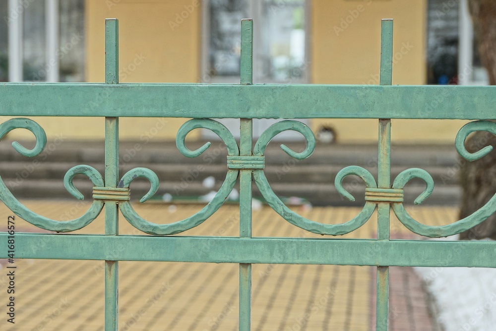 Wall mural metal texture from a green forged pattern on bars of a fence on the street against a brown backgroun