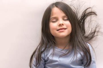 Beautiful little girl with long hair and open mouth on a white background looks down. Preschooler...