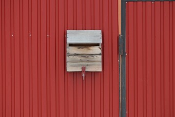 one gray wooden mailbox hanging on a red metal fence wall in the street