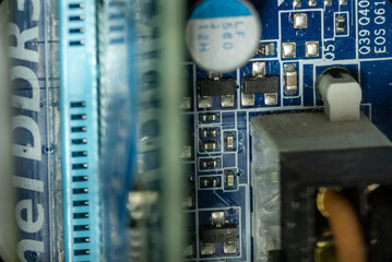 several microcircuits and transistors near connectors with wires and slots for RAM on the motherboard in a dusty personal computer close-up