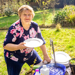 Plump mature woman washes dishes in her garden