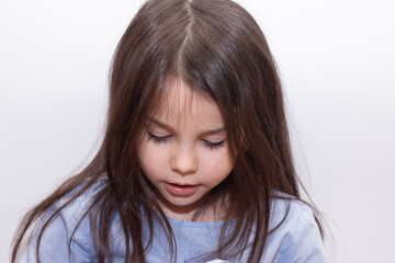 The preschooler child looks down with his mouth parted. Studio photo of a little beautiful girl on a white background.