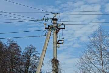 concrete pillar with many electrical wires against the background of blue sky and clouds and gray...