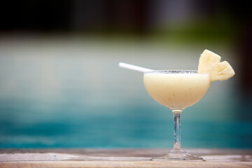 Glass of pinacolada cocktail standing on the swimming pool