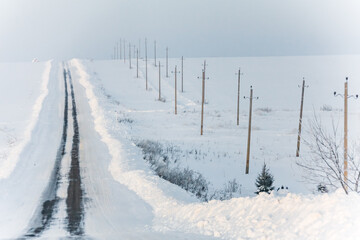 Winter landscape. Empty highway covered with snow in the countryside. The rhythms of the pillars in the field. Frosty weather.