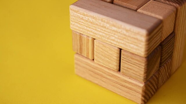Video logical wooden puzzle puzzle close up on a yellow background, the hand puts the last element. High quality FullHD footage