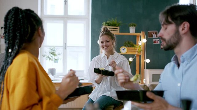 Group of friends eating take away food indoors, food delivery and house sharing concept.