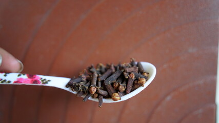 A person holding a cloves spoon on his hand. Indian dry clove spices on red background
