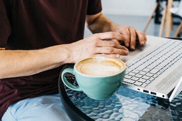 Freelance lifestyle concept Close up young man hands on the table with laptop, cappuccino and croissant in cafe.