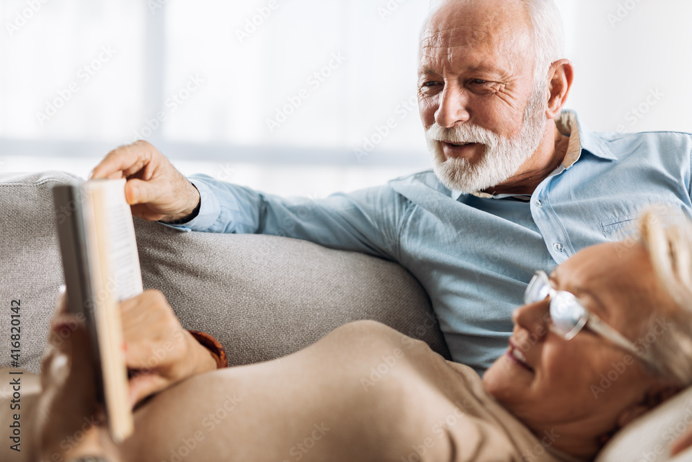 Wall mural mature couple resting on their sofa at home and reading a book together