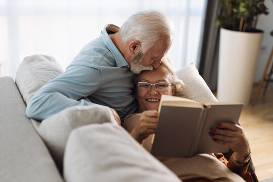 Mature man kissing his wife while reading a book togehther at home