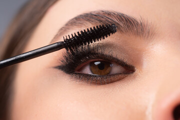 Closeup of eye makeup. Applying maskara on lushes Young woman getting make up with brush. Eyes...