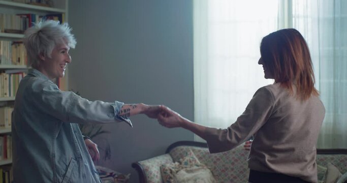 Cinematic shot of young carefree happy smiling homosexual female gay and transgender man couple in love is enjoying time together and having fun to dance together while listening to the music at home