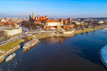 Fototapeta na wymiar Krakow, Poland. Aerial skyline with Royal Wawel castle and cathedral. Vistula river, tourist boats, parks, promenades, walking people and swans in winter at sunset