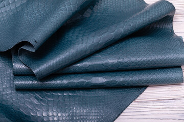 Blue-gray dyed genuine natural python skin folded on a wooden table.