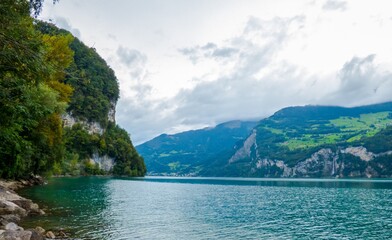 Naklejka na ściany i meble Lago Walensee con sus orillas que mezclan roca y vegetación, en un día núblado típico del verano suizo