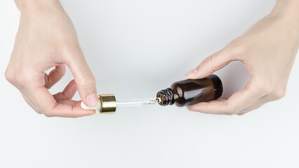 Female hands holding glass bottle of beauty serum with liquid drop. Beauty product for skincare concept