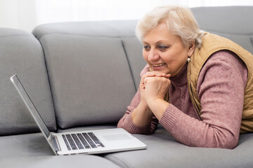 Elderly woman making video call on laptop, waving at screen, chatting with children, free space