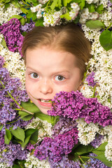 Funny little girl holding flowers in blooming summer garden. Teenager girl with bouquet of purple and white lilac.