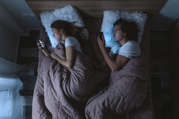 Fototapeta na wymiar Top view of young couple lying in bed at night and using smartphones