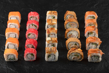 Set of delicious traditional sushi rolls on black surface