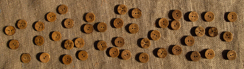 Variety of ethnic tribal African boho brown coconut buttons on brown rustic linen fabric. A horizontal pattern background for website leaderboard, social network group header or banner