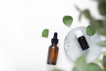 Essential oil with eucalyptus branches on white background with copy space top view. Brown glass cosmetic bottle, serum.